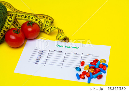 Diet plan for weight loss pills and fresh vegetables on yellow background. 63865580