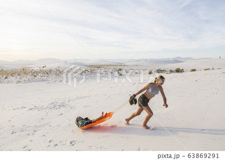 A teenage girl pulling her brother in sled at sunset, 63869291