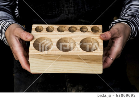 Close up of person holding wooden block with circular holes in different sizes. 63869695