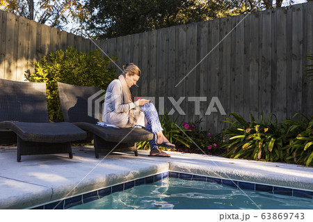 Woman sitting on sun lounger by a swimming pool 63869743