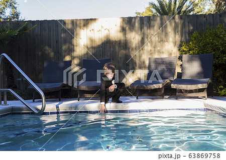 A young boy wearing black suit and bow tie standing by a swimming pool 63869758