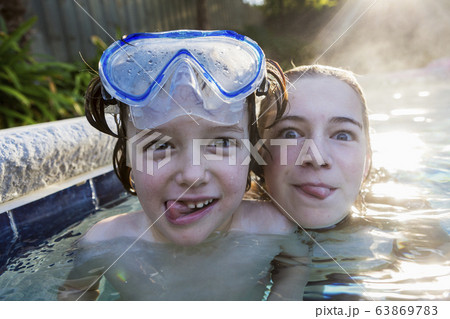 A teenage girl and brother in a warm pool, looking at the camera, sticking their tongues out. 63869783