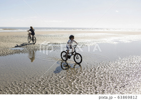 Two children cycling on an open beach, a boy and girl. 63869812