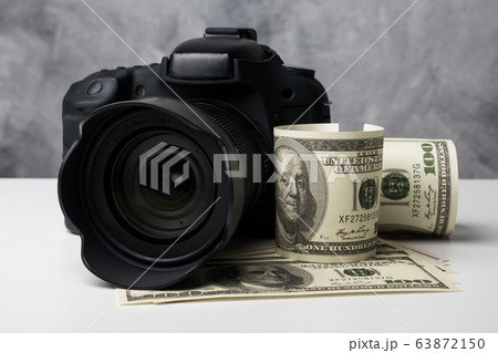 A black digital camera and banknotes on a white table with grunge background. A black digital camera and banknotes on a white table with grunge background. 63872150