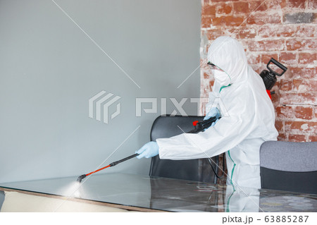 Coronavirus Pandemic. A disinfector in a protective suit and mask sprays disinfectants in the house or office Coronavirus Pandemic. A disinfector in a protective suit and mask sprays disinfectants in the house or office 63885287