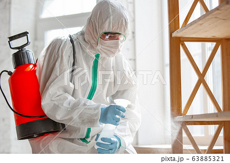 Coronavirus Pandemic. A disinfector in a protective suit and mask sprays disinfectants in the house or office 63885321