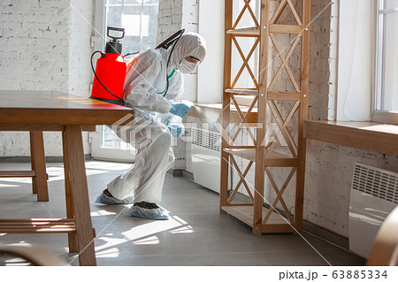 Coronavirus Pandemic. A disinfector in a protective suit and mask sprays disinfectants in the house or office Coronavirus Pandemic. A disinfector in a protective suit and mask sprays disinfectants in the house or office 63885334