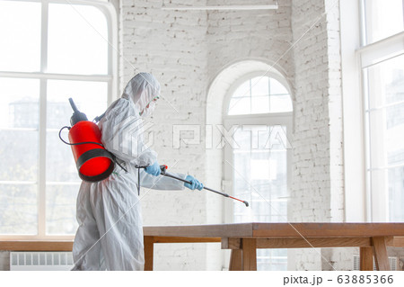 Coronavirus Pandemic. A disinfector in a protective suit and mask sprays disinfectants in the house or office Coronavirus Pandemic. A disinfector in a protective suit and mask sprays disinfectants in the house or office 63885366