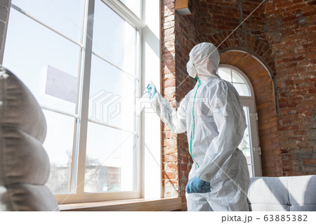 Coronavirus Pandemic. A disinfector in a protective suit and mask sprays disinfectants in the house or office 63885382