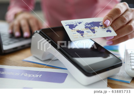 Girl at table holds credit card over bank terminal Girl at table holds credit card over bank terminal 63885733