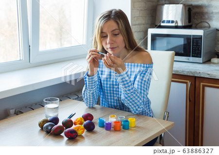 Holidays, handmade and creation concept - Happy young woman draws on Easter egg. Holidays, handmade and creation concept - Happy young woman draws on Easter egg. 63886327