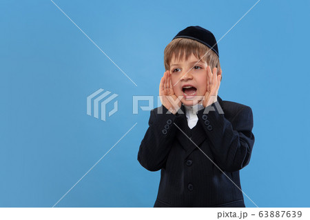 Portrait of a young orthodox jewish boy isolated on blue studio background, meeting the Passover Portrait of a young orthodox jewish boy isolated on blue studio background, meeting the Passover 63887639