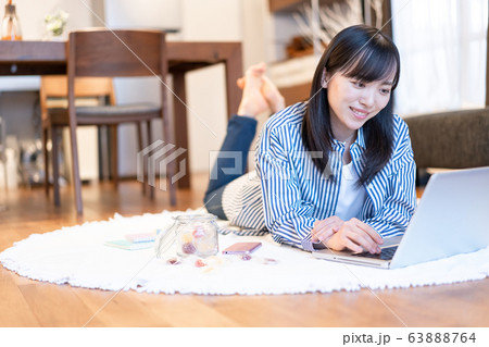 リビングで横になりながらネットをする若い女性 63888764