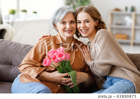 Happy woman hugging aged mother with flowers. 63890875