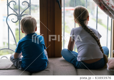 Stay at home quarantine coronavirus pandemic prevention, brother and sister looking out the window unable to go out for a walk 63893976