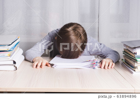 Tired schoolboy lying on the table clutching his Tired schoolboy lying on the table clutching his 63894896