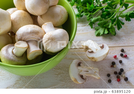 Whole raw fresh champignons in a green bowl near bunch of parsley on a wooden table. 63895120
