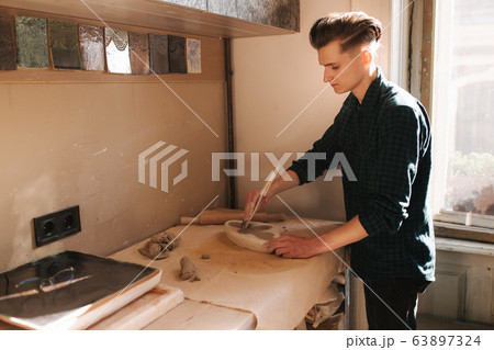 Man potter looking for ware for a work. Young man potter in his workshop. Handsome man work Man potter looking for ware for a work. Young man potter in his workshop. Handsome man work 63897324
