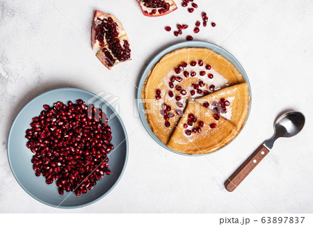Grains of peeled pomegranate lie in a plate. Pancakes with pomegranate and condensed milk lie on a plate. View from above. Close-up. 63897837