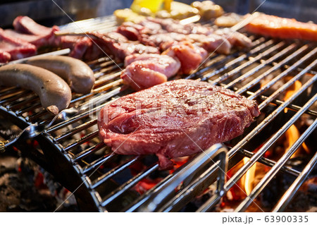 The meat is pickled on a lattice grill, ribs spread, a stake, Sausages, edges, chicken, naked flame, black pepper, a smoke, firewood, light reflections, close up The meat is pickled on a lattice grill, ribs spread, a stake, Sausages, edges, chicken, naked flame, black pepper, a smoke, firewood, light reflections, close up 63900335
