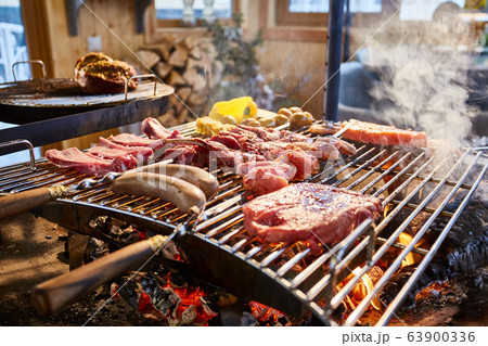 The meat is pickled on a lattice grill, ribs spread, a stake, Sausages, edges, chicken, naked flame, black pepper, a smoke, firewood, light reflections, close up The meat is pickled on a lattice grill, ribs spread, a stake, Sausages, edges, chicken, naked flame, black pepper, a smoke, firewood, light reflections, close up 63900336