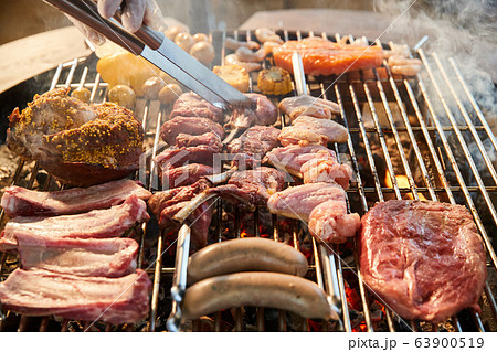 The meat is pickled on a lattice grill, ribs spread, a stake, Sausages, edges, chicken, naked flame, black pepper, a smoke, firewood, hands of the chef display meat, Hands in gloves, close up 63900519