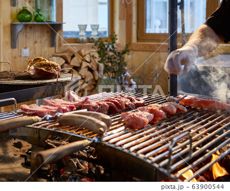The meat is pickled on a lattice grill, ribs spread, a stake, Sausages, edges, chicken, naked flame, black pepper, a smoke, firewood, hands of the chef display meat, Hands in gloves, close up The meat is pickled on a lattice grill, ribs spread, a stake, Sausages, edges, chicken, naked flame, black pepper, a smoke, firewood, hands of the chef display meat, Hands in gloves, close up 63900544