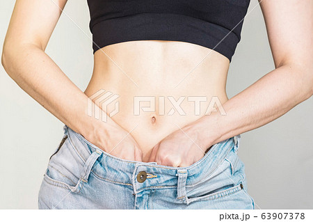 woman with thin waist,tightened up,wore jeans loose waist, holding pink measuring tape,health care concept woman with thin waist,tightened up,wore jeans loose waist, holding pink measuring tape,health care concept 63907378