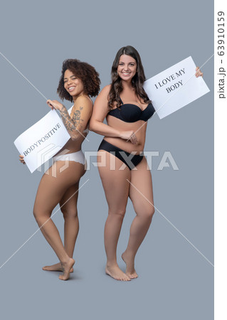 Girlfriends in linen barefoot with posters calling for self-perception. 63910159