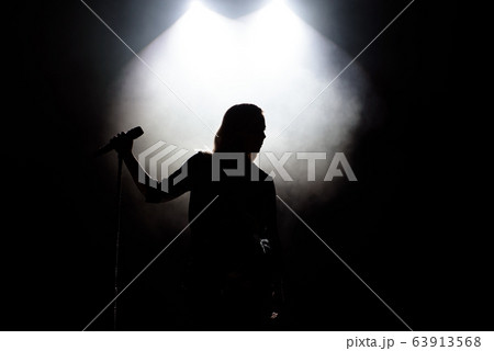 black silhouette of female singer with white spotlights in the background 63913568