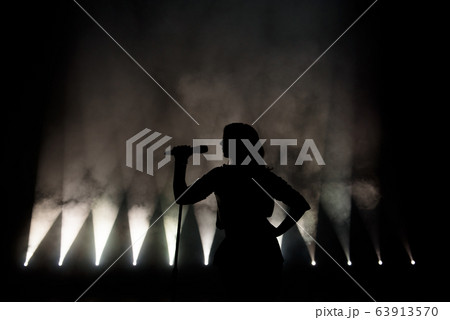 black silhouette of female singer with white spotlights in the background 63913570