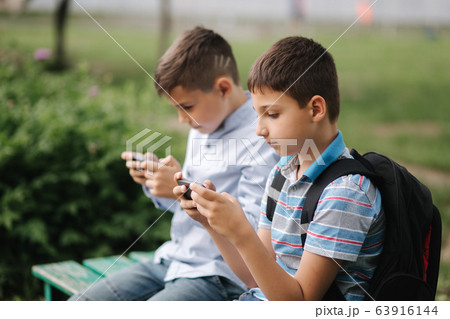Two boy sitting on the bench and play online games. One boys with backpack. Young boys use their phones. Quarantine 63916144