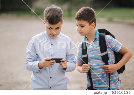 Two boys plays online games in quarantine. Young boys smile and use phone Two boys plays online games in quarantine. Young boys smile and use phone 63916159