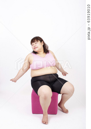 白い背景の前でピンクの椅子に座って目をつぶり深呼吸をしている太った若い女性 白い背景の前でピンクの椅子に座って目をつぶり深呼吸をしている太った若い女性 63919010