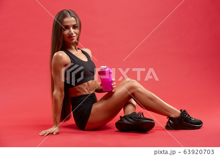 Fitnesswoman sitting with shaker on studio floor. 63920703