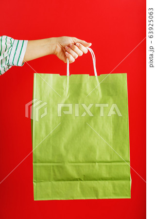 Green paper bag at arm's length isolated on a red Green paper bag at arm's length isolated on a red 63925063