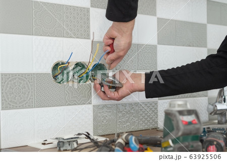 Renovation and construction in kitchen, close-up of electricians hand installing outlet on wall with ceramic tiles using professional tools Renovation and construction in kitchen, close-up of electricians hand installing outlet on wall with ceramic tiles using professional tools 63925506