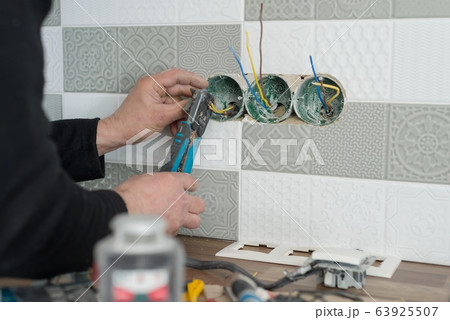 Renovation and construction in kitchen, close-up of electricians hand installing outlet on wall with ceramic tiles using professional tools Renovation and construction in kitchen, close-up of electricians hand installing outlet on wall with ceramic tiles using professional tools 63925507