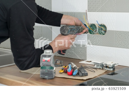 Renovation and construction in kitchen, close-up of electricians hand installing outlet on wall with ceramic tiles using professional tools Renovation and construction in kitchen, close-up of electricians hand installing outlet on wall with ceramic tiles using professional tools 63925509