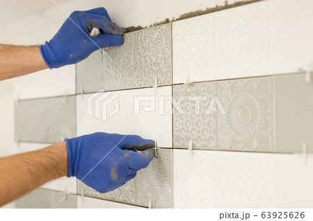 Installing ceramic tiles on the wall in kitchen. Placing tile spacers with hands, renovation, repair, construction 63925626