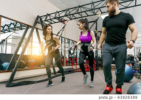 Fitness trainer coaching and helping women doing exercises on cross fit using straps system in gym. Sport, teamwork, people concept. Fitness trainer coaching and helping women doing exercises on cross fit using straps system in gym. Sport, teamwork, people concept. 63926389