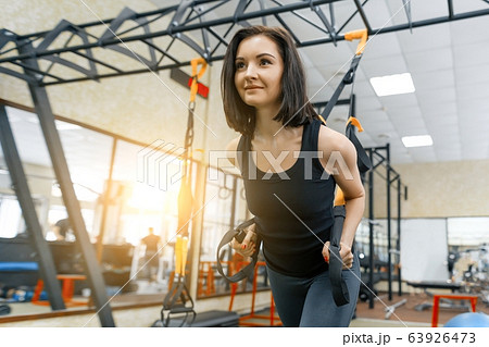 Young woman at the gym doing fitness exercises using sports straps system, holding hands by the loops. Fitness, sport, training, people concept. Young woman at the gym doing fitness exercises using sports straps system, holding hands by the loops. Fitness, sport, training, people concept. 63926473