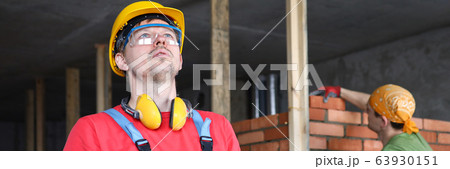 Builder in overalls and helmet makes notes folder 63930151