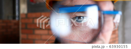 Builder in helmet looks through magnifying glass 63930155