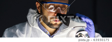 Man in protective clothing examines microscope 63930175