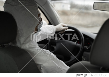 Man in protective suit, medical mask and rubber gloves for protect from bacteria and virus is driving a car. Protective mask while quarantine, world pandemic, covid 19, coronavirus, infection. Man in protective suit, medical mask and rubber gloves for protect from bacteria and virus is driving a car. Protective mask while quarantine, world pandemic, covid 19, coronavirus, infection. 63935309