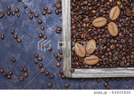 Composition with roasted coffee beans and coffe bean shaped cookies on dark brown background Composition with roasted coffee beans and coffe bean shaped cookies on dark brown background 63935930