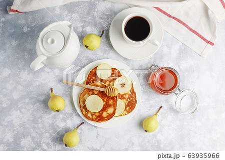 Homemade breakfast: american style pancakes served with pears and honey with a cup of tea on concrete background. Top view and copy space Homemade breakfast: american style pancakes served with pears and honey with a cup of tea on concrete background. Top view and copy space 63935966