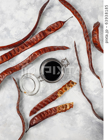 Carob syrup in glass jar with carob pods and seeds on light background Carob syrup in glass jar with carob pods and seeds on light background 63938185