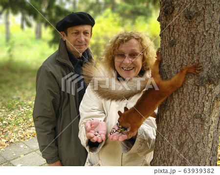 Happy smiling senior citizens feed a squirrel in the park. 63939382